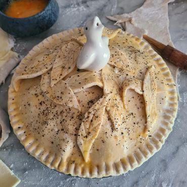 Unbaked pie with decorative leaf patterns and a bird-shaped vent on top.