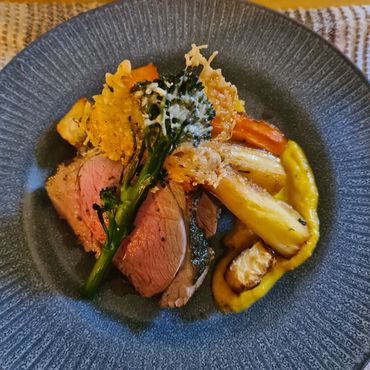 Elegant dish with roasted meat, vegetables, and crispy cheese on a textured gray plate.