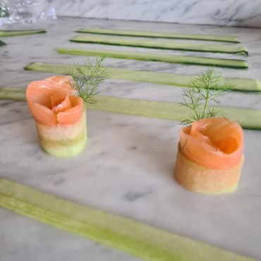 Delicate smoked salmon roses with cucumber ribbons and dill garnish on marble.