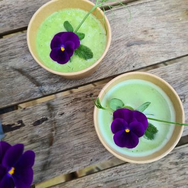 Two green smoothies with purple edible flowers on a wooden table.