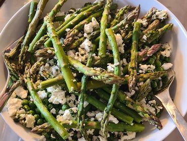 Fresh asparagus salad with crumbled cheese and herbs in a white bowl.