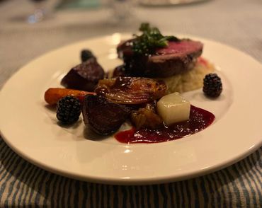 Gourmet plate with steak, roasted vegetables, blackberries, and sauce.