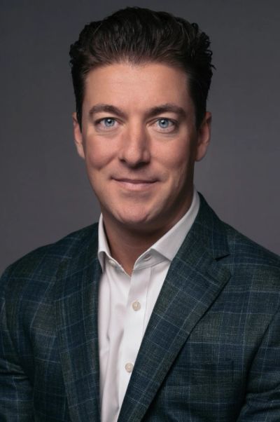 Professional portrait of a man in a checkered blazer and white shirt.