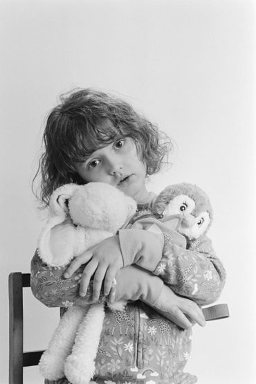 Young child hugging two stuffed animals, looking thoughtful.