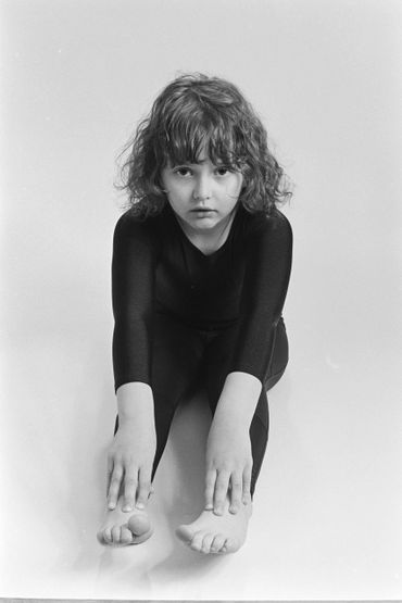 Black and white photo of a young girl stretching forward touching her feet.