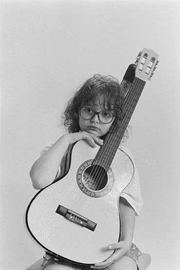 Young girl with glasses holding an acoustic guitar, looking thoughtful.