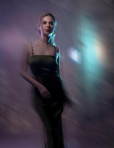 Woman in a sleek dress illuminated by soft, colorful lighting.