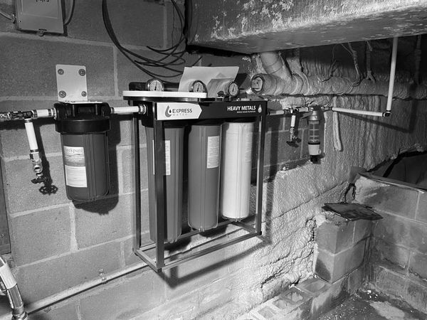 Water filtration system labeled 'Heavy Metals' installed on a basement wall.