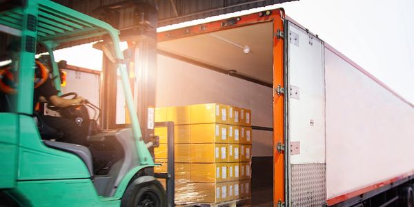 Forklift loading yellow boxes into a truck at sunset.