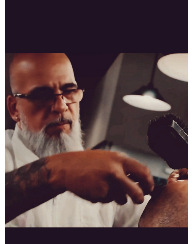 Barber with glasses and a beard giving a haircut in a barbershop.