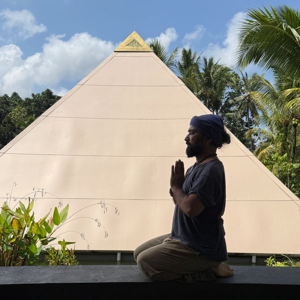 Man meditating in front of a pyramid-shaped structure.