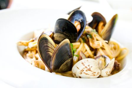 A clam seafood pasta dish in a white bowl. 