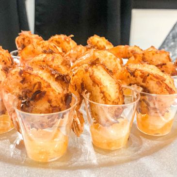 Crispy coconut shrimp displayed in clear shot glasses containing range marmalade dipping sauce