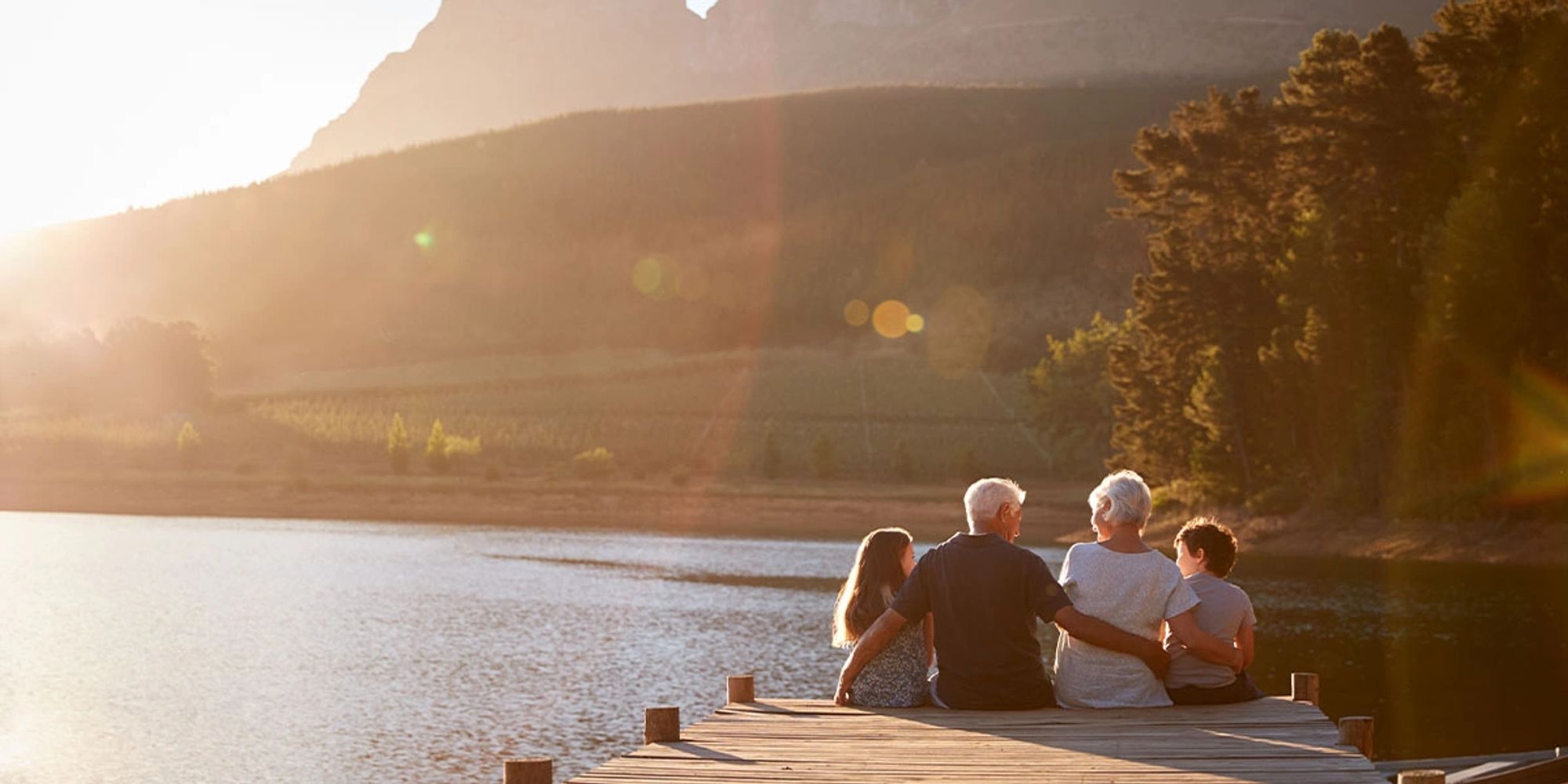 Family of four sitting on a dock by a lake at sunset.