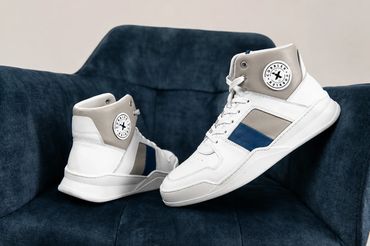White CobblerX high-top sneakers with grey and blue panels displayed on a dark blue chair.