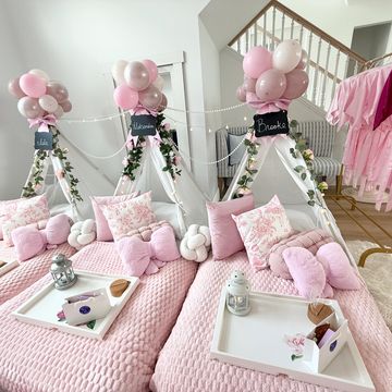 Cozy pink-themed indoor teepee setup with balloons and plush pillows for a sleepover.