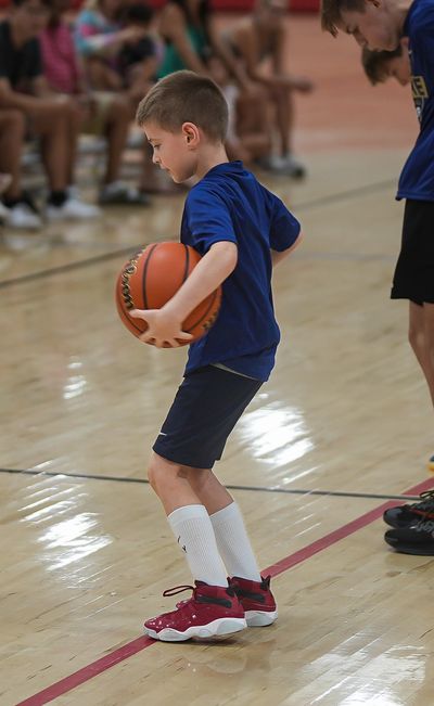 A young boy in blue shirt practicing basketball on indoor court.