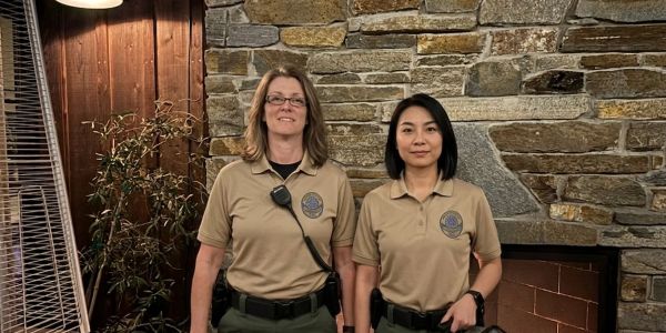 Two security officers standing indoors by a stone wall.