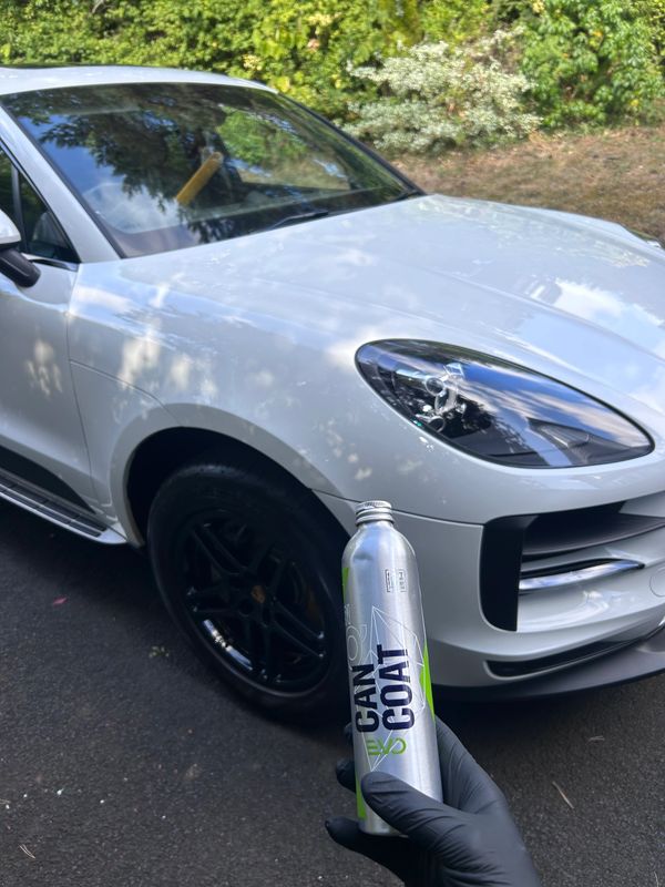 A silver car with a black wheel and a metallic bottle held in front.