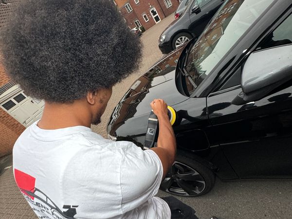 Man polishing a black car with a buffer in a driveway.