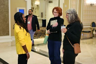 Three women engaged in conversation in a bright hallway.