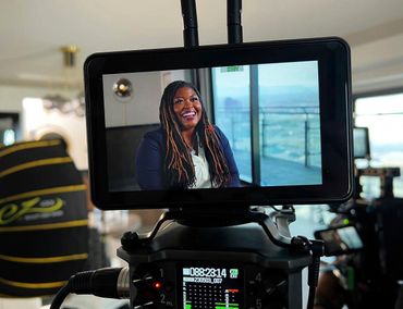A woman smiles during a video interview displayed on a camera screen.