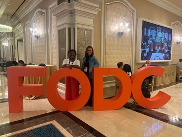 Two women posing behind large orange letters spelling FODC in a luxurious hallway.