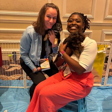 Two women happily holding puppies inside a playpen area with blue mats.