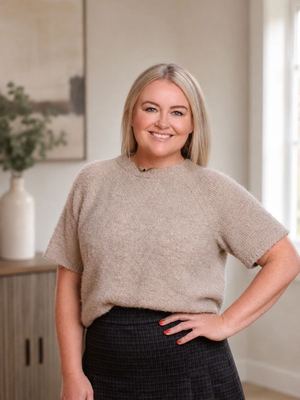 Smiling woman in beige sweater and dark skirt.