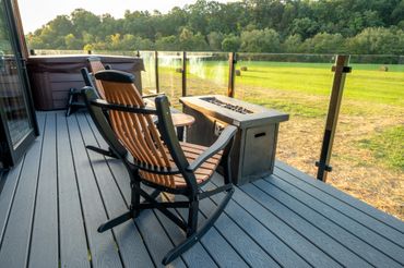View towards river over field from deck w/ adirondack rocking chairs, gas firepit, & hot tub.