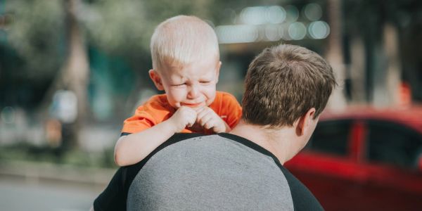 A toddler crying on an adult's shoulder.
