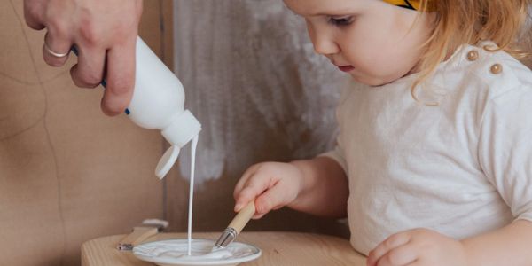 Toddler watches as adult pours glue on a plate.