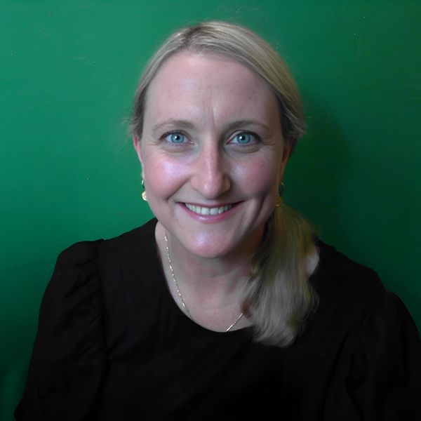 Karin wearing a black top and her blonde hair in a ponytail looking straight at the camera.