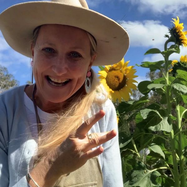 A picture of Karin wearing an Akubra hat outside standing in front of sunflowers on a sunny day sign