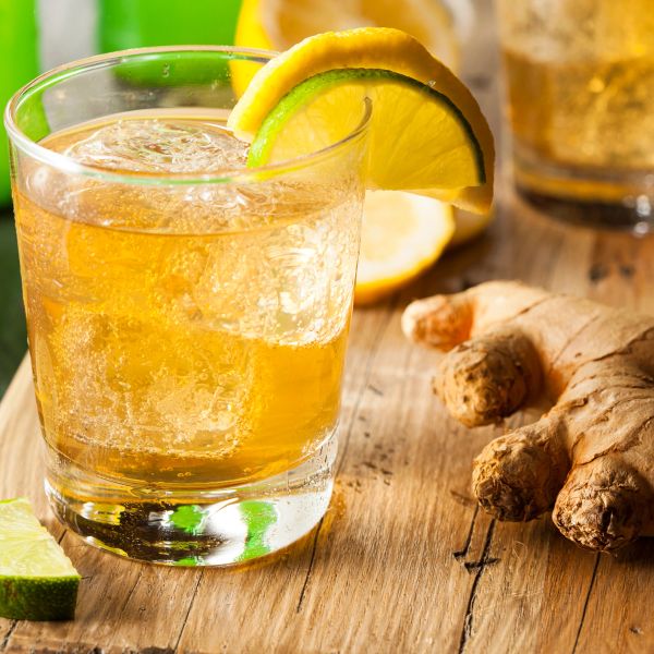 A glass of ginger ale with ice and lemon-lime garnish on a wooden surface.