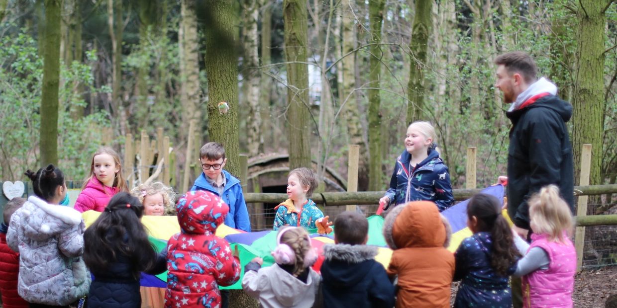 Children and an adult playing with a colorful parachute in a forest.