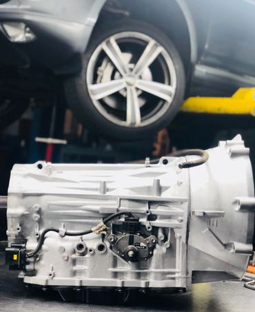 Close-up of a car transmission on a workshop table with a car wheel in the background.