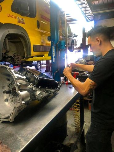A mechanic works on an engine part in a garage with vehicles on lifts.