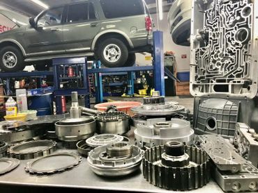 Car transmission parts laid out in an auto repair shop with an SUV on a lift.