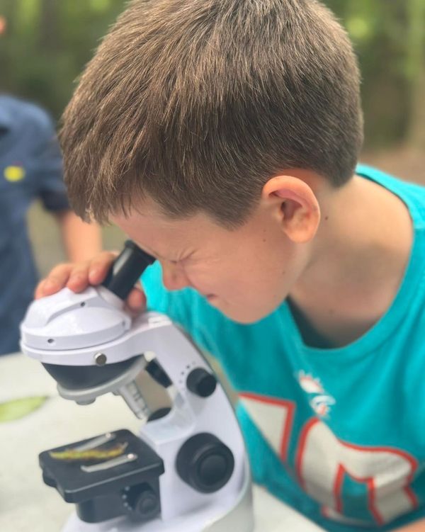 A young boy closely examining a specimen through a microscope outdoors.