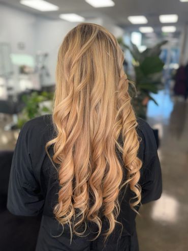 Long, blonde hair styled in loose curls against a blurred salon background.