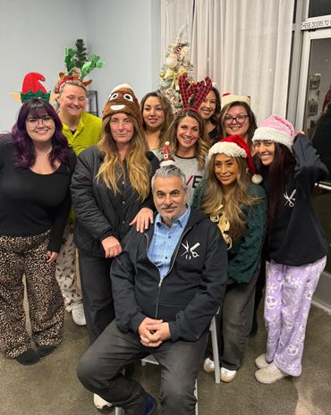 Group of people in festive holiday hats posing indoors by a decorated Christmas tree.