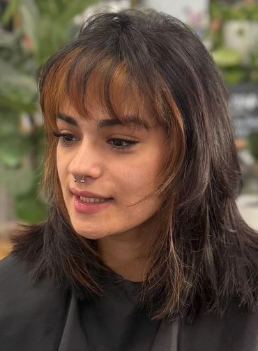 Young woman with layered brown hair and orange highlights at a salon.