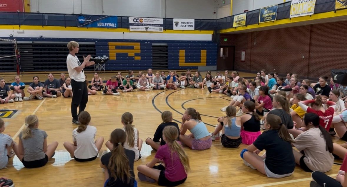 Dana coaching a positive mindset to young volleyball players seated in a gym.