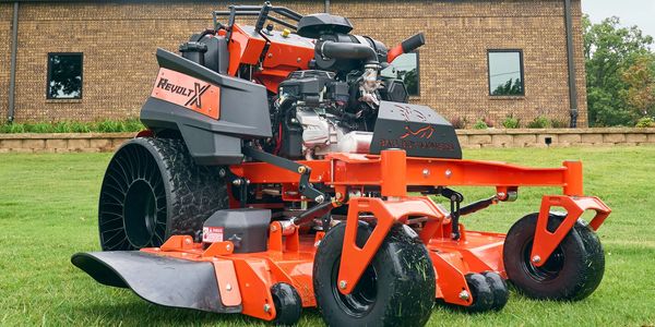 Orange lawn mower on grass near brick building.