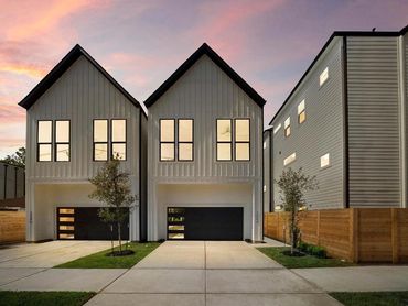 Two modern white houses with black garage doors at sunset.