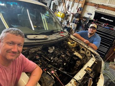 Two men working on a car engine in a garage.