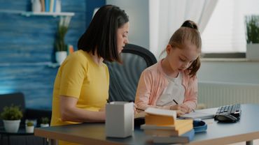 Woman helping young girl with homework at a desk.