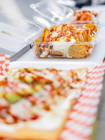 Close-up of nachos with toppings in a clear plastic container.