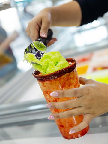 A person scoops bright green ice cream into a spicy-rimmed cup.